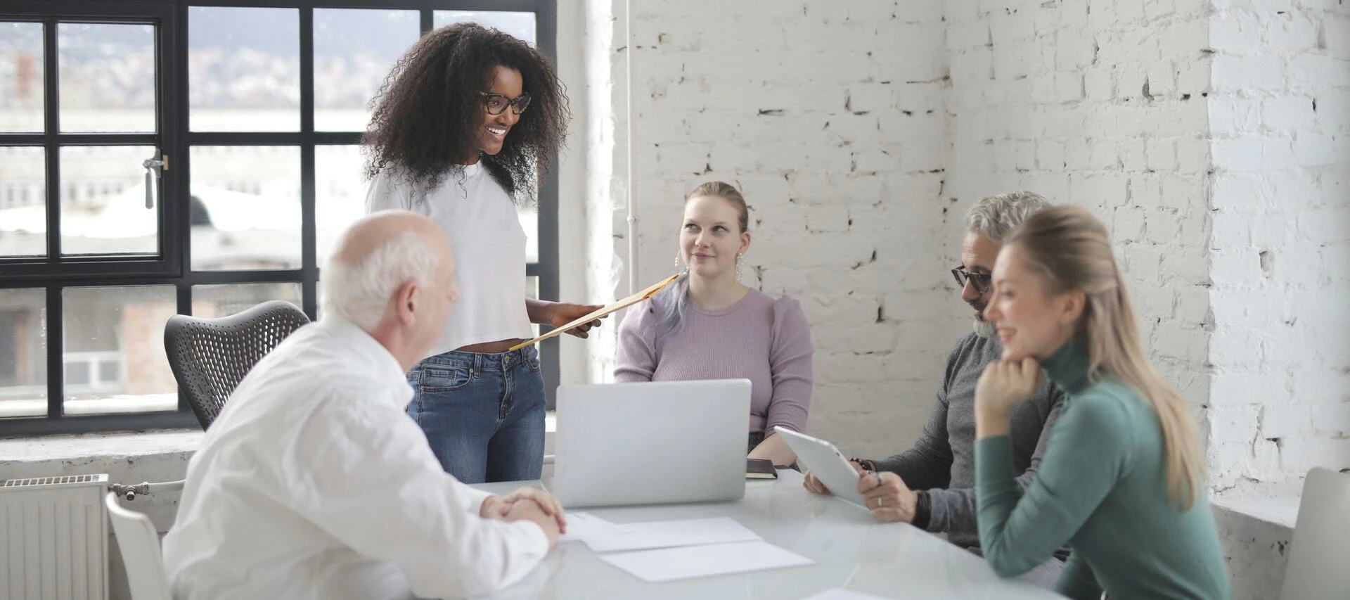 employees sitting in a meeting and listening to a woman speaking with paper in her hand