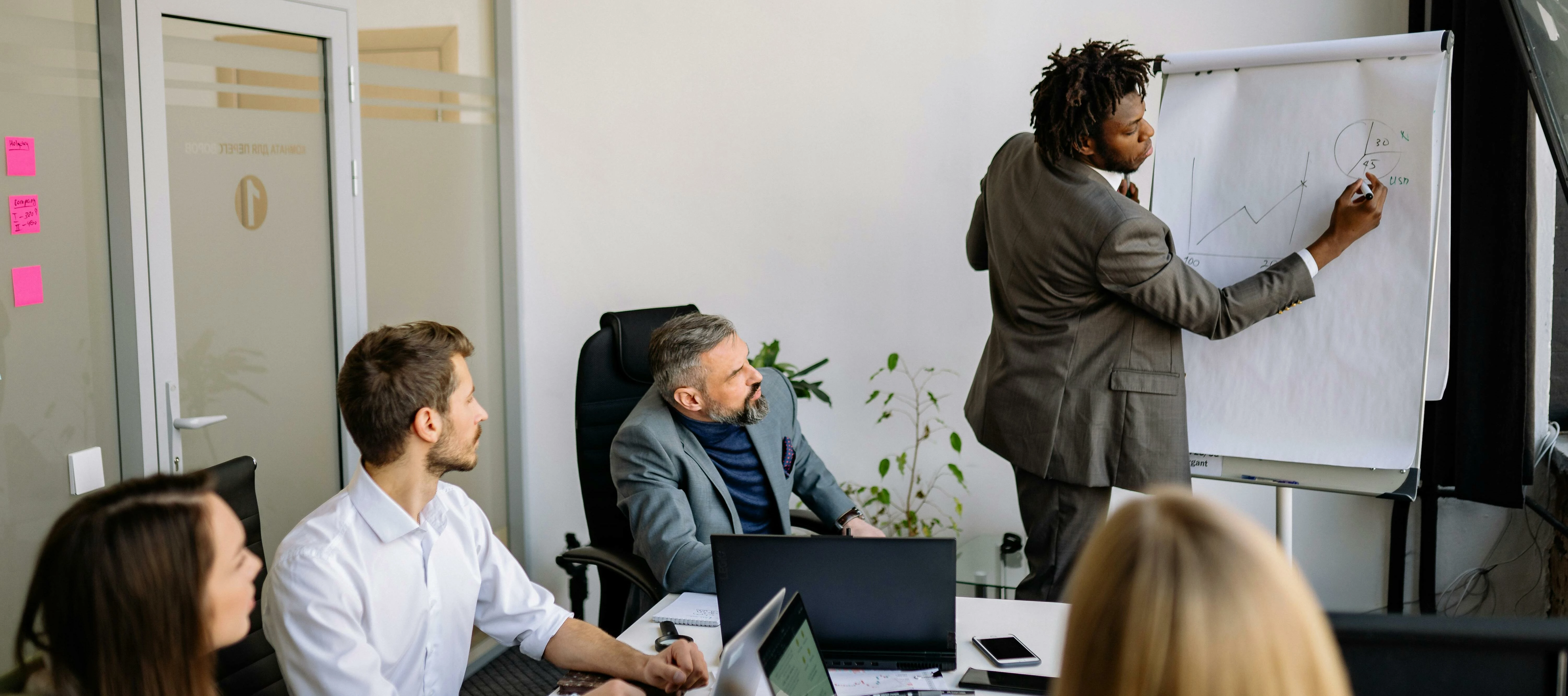 man presenting results to a team in a meeting with laptops