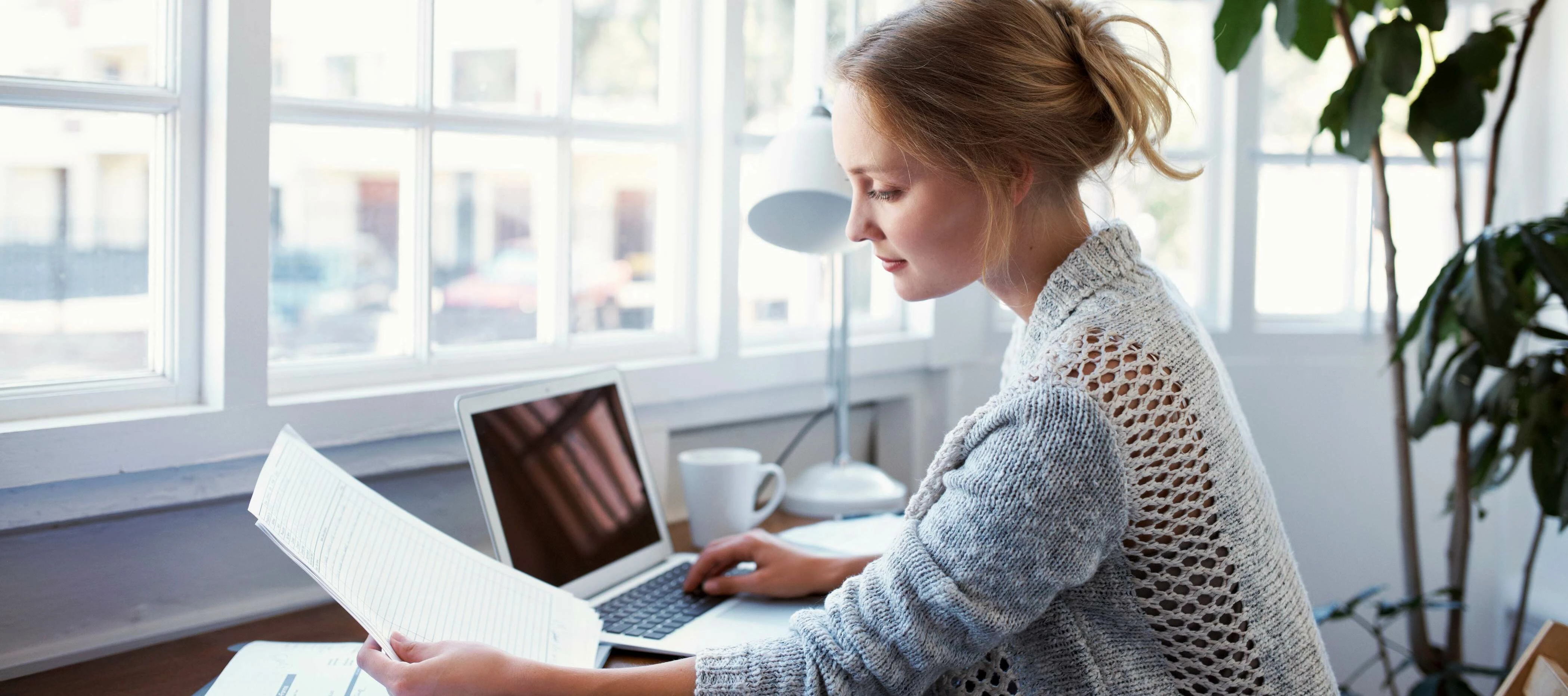 woman at her desk reviewing paperwork in front of laptop