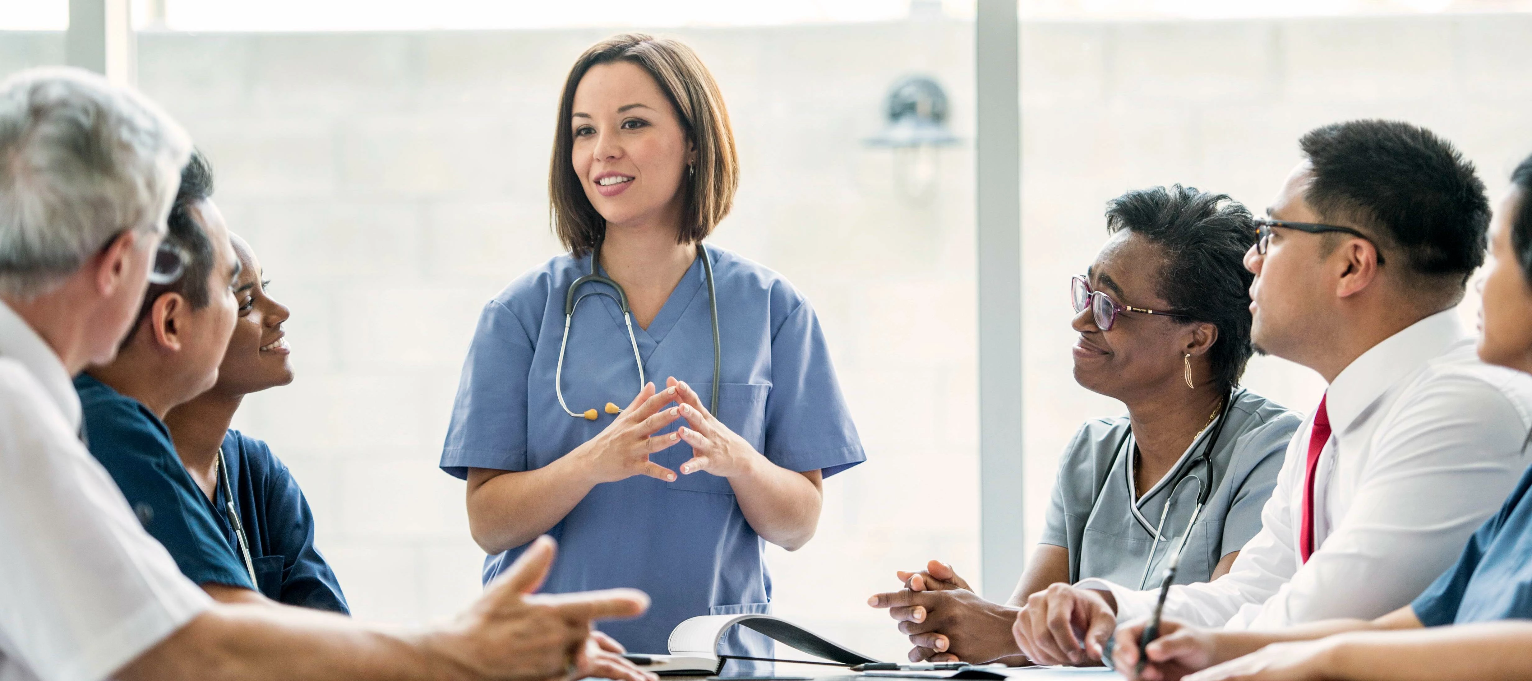 Nurse with stethoscope speaking to doctors and executives during a meeting