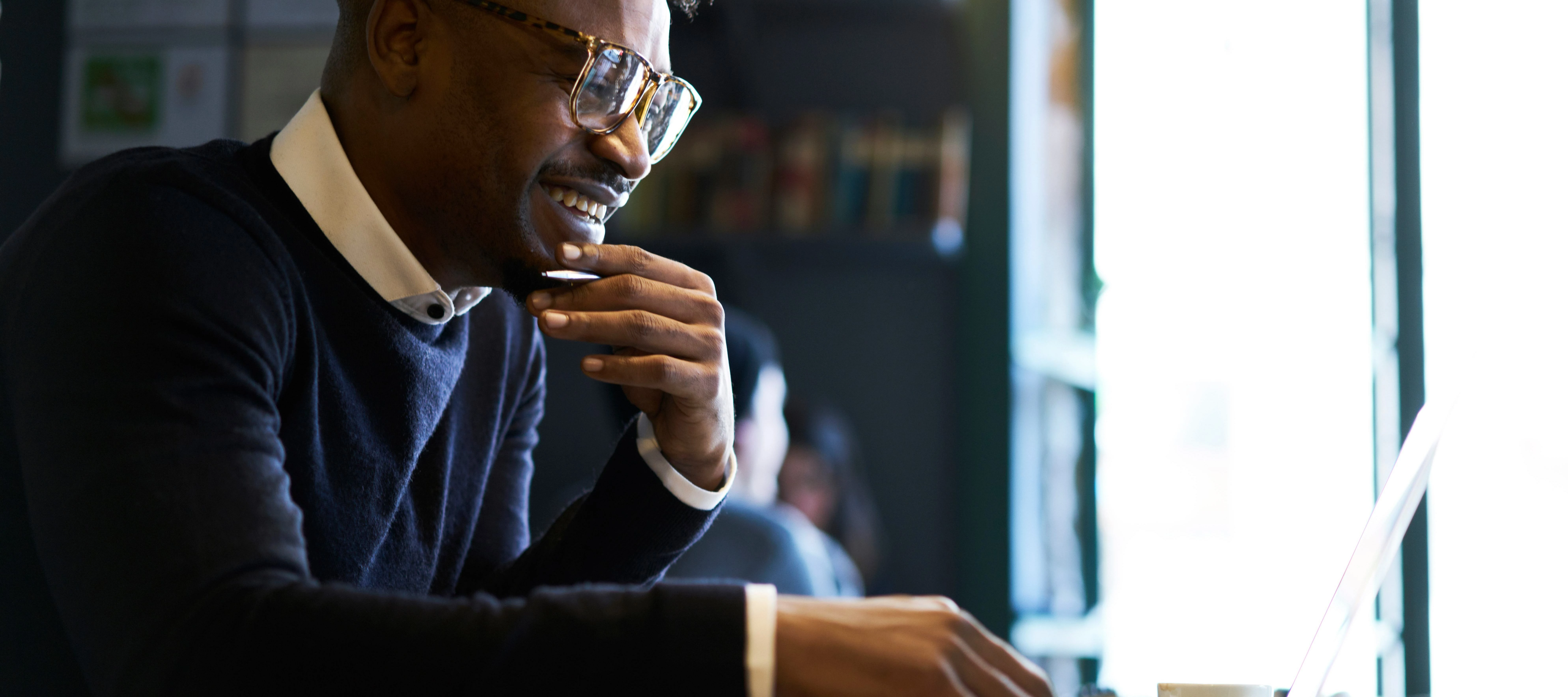 person with glasses smiling while he works on his laptop