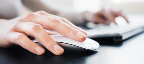Hand holding a computer mouse and working on laptop