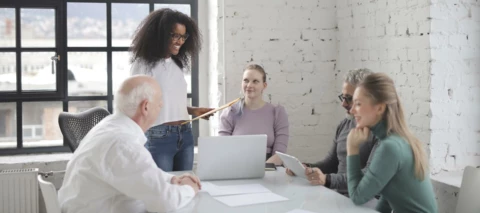 employees sitting in a meeting and listening to a woman speaking with paper in her hand