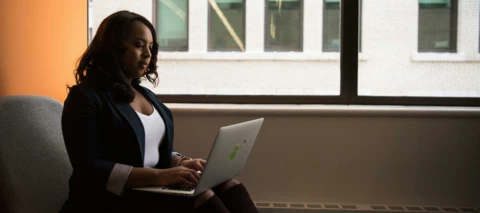 women typing on a laptop in front of a window