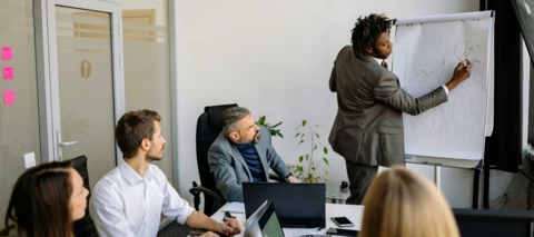 man presenting results to a team in a meeting with laptops