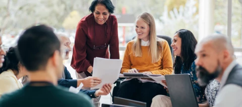 employees with laptops and smiling while looking at paperwork and results