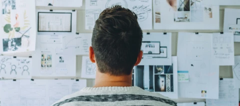 man thinking while looking at a board with graphs, paper, and information