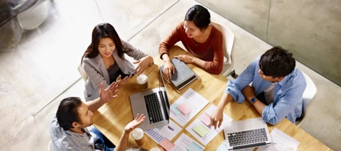 Group of coworkers with laptops and paperwork a desk conversing